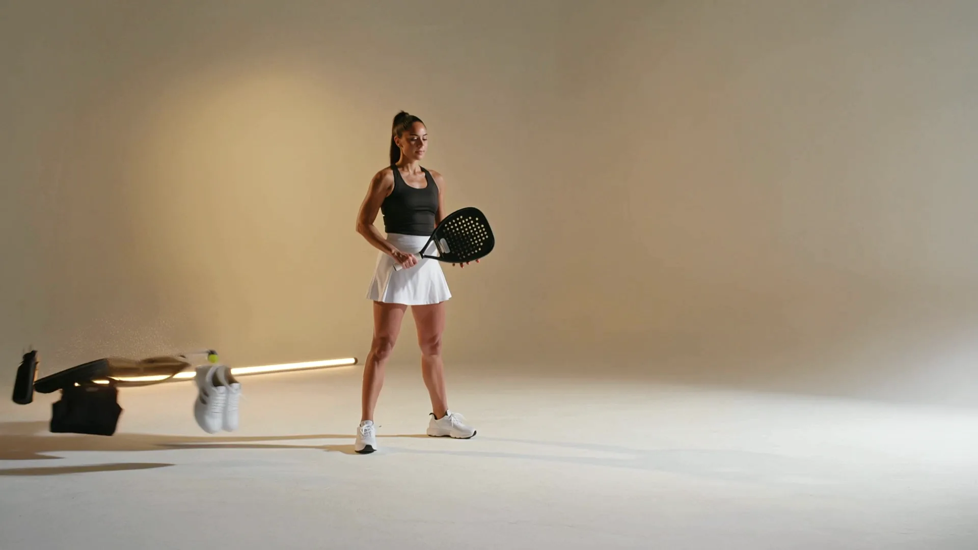 Une joueuse en mouvement dans une scène éclairée aux tons sable, entourée de raquettes, chaussures et vêtements de padel.